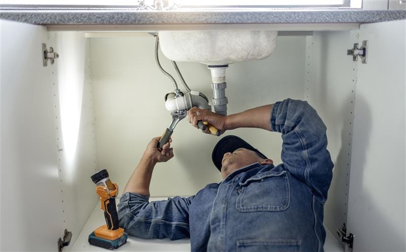 Plumber repairing pipes beneath a bathroom sink in Culver City
